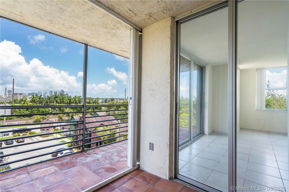 View from a balcony with glass doors and railings overlooking trees and distant buildings.