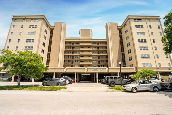 Front view of a mid-rise residential building with multiple balconies and a parking area in front.