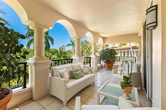 View from a covered balcony with archways and outdoor seating, overlooking tropical surroundings.