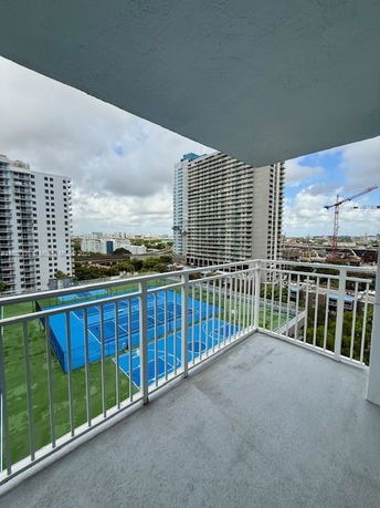 View from a balcony overlooking tall buildings and tennis courts.