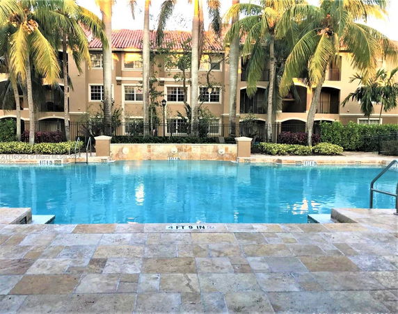 View of a swimming pool with surrounding palm trees and a building in the background.