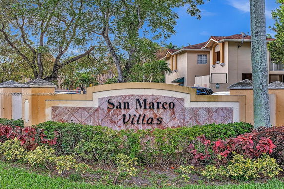 Entrance sign for San Marco Villas with trees and a building in the background.