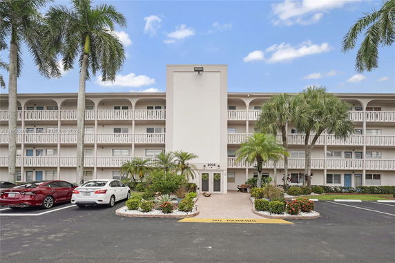 Front view of a multi-story residential building with balconies and palm trees.