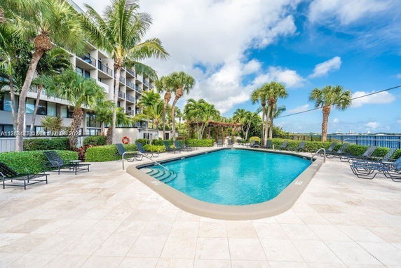 Outdoor swimming pool area with lounge chairs and surrounding palm trees.