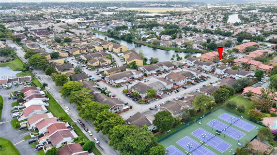 Panoramic aerial view of a residential neighborhood with houses, a waterway, and tennis courts.