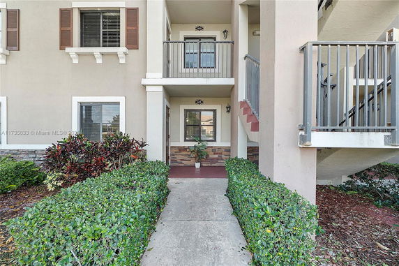 Front view of a residential building entrance with two floors and surrounding plants.