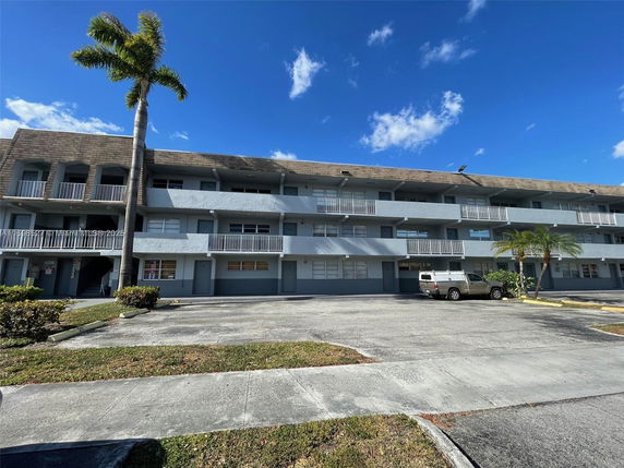 Front view of a multi-story building with balconies and parking area.