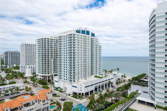 Aerial view of modern high-rise buildings near the coastline, featuring white facades and numerous balconies.