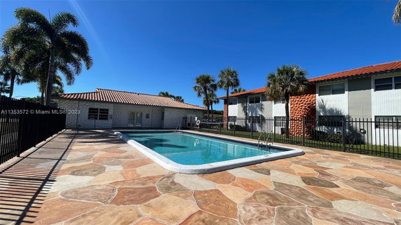 Outdoor swimming pool area with a surrounding paved deck and nearby buildings.