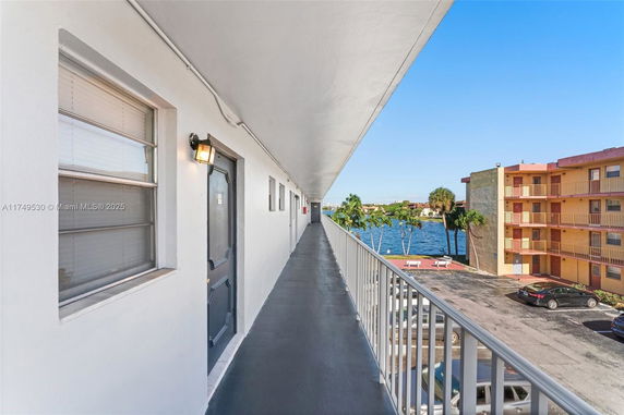 Outdoor corridor of a residential building overlooking a water body and parking area.