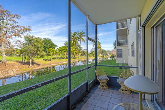 View from a building's screened balcony overlooking a grassy area with trees and a waterway.