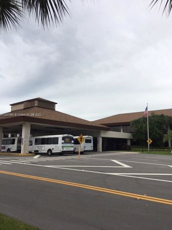 Front view of a large building with a covered entrance and buses parked in front.