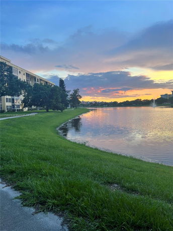 View of a lake with a building on the left and trees along the shore at sunset.