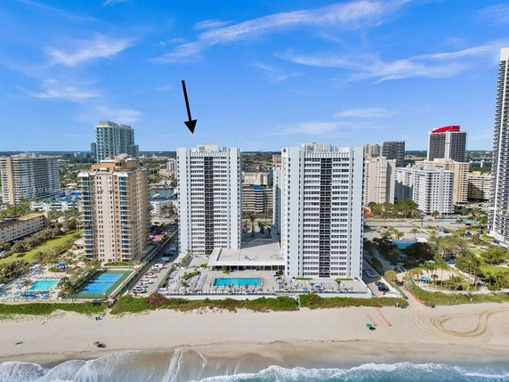 View of a beachfront apartment complex with multiple tall buildings and surrounding urban area.