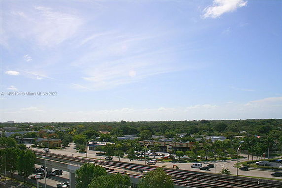 Panoramic view showing a rail line, road, and trees with a clear sky.