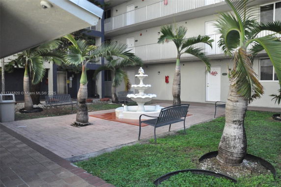 Courtyard with palm trees, benches, and a central fountain surrounded by a multi-story building.