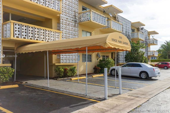 Parking area in front of a multi-story building with distinctive patterned balconies and an awning entrance.