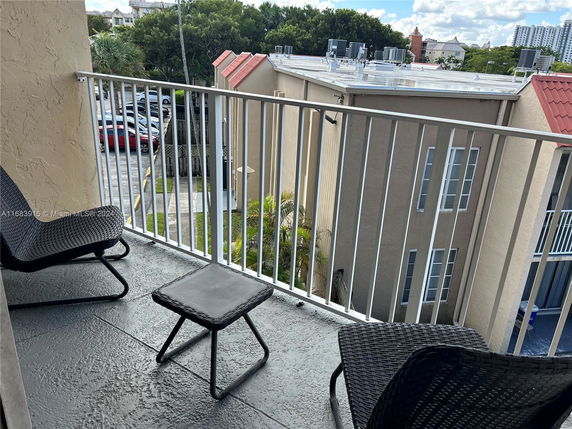 View from a balcony overlooking nearby buildings and a parking area.