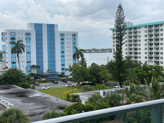 View from building balcony of nearby residential buildings with blue and white facades and a body of water in the background.