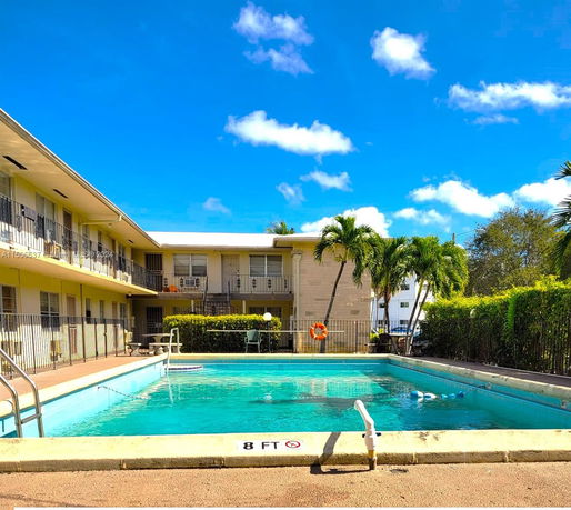 Outdoor swimming pool adjacent to a multi-story building with balconies.