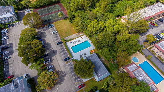 Aerial view of swimming pool, parking lot, tennis court, and surrounding greenery.