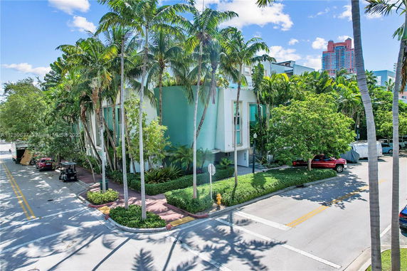 Front view of a modern two-story building with a green facade, surrounded by palm trees.