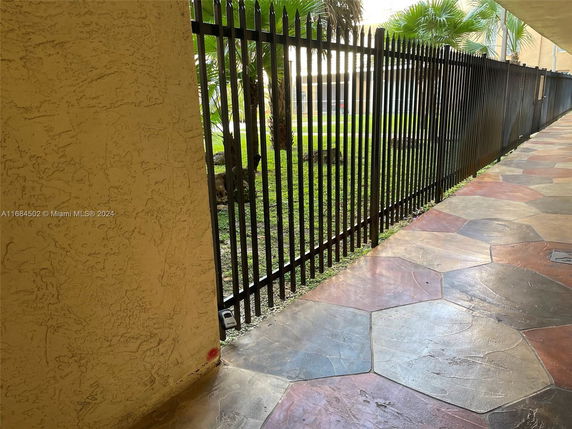 View of walkway with decorative pavement next to a wrought iron fence and greenery.
