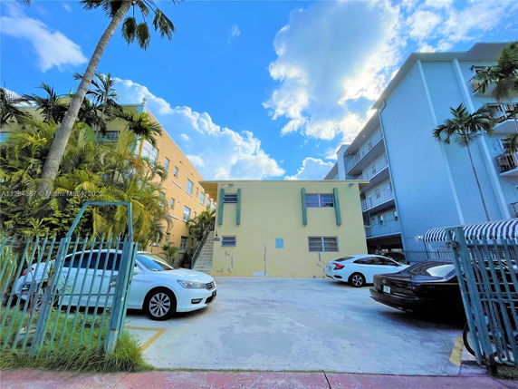Outdoor parking area in front of a yellow building with multiple vehicles parked.