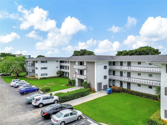 Front view of a multi-story apartment building with balconies and surrounding parking area.