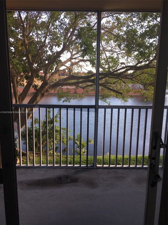 Balcony view overlooking a lake with trees and distant buildings.