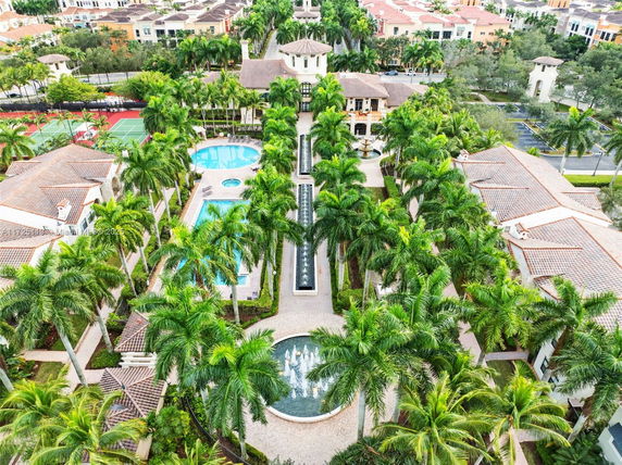 Aerial view of a landscaped area with palm-lined paths, swimming pools, and residential buildings.