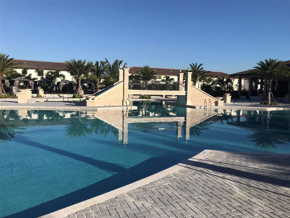 Large outdoor swimming pool with a bridge and surrounding palm trees.