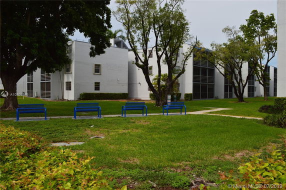 View of a multi-story building with white exterior walls and large windows, surrounded by trees and grass.