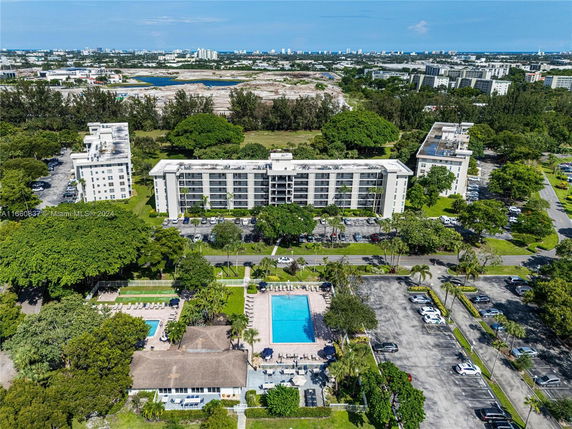 Aerial view of multiple apartment buildings with a large swimming pool and parking lots in a residential area.
