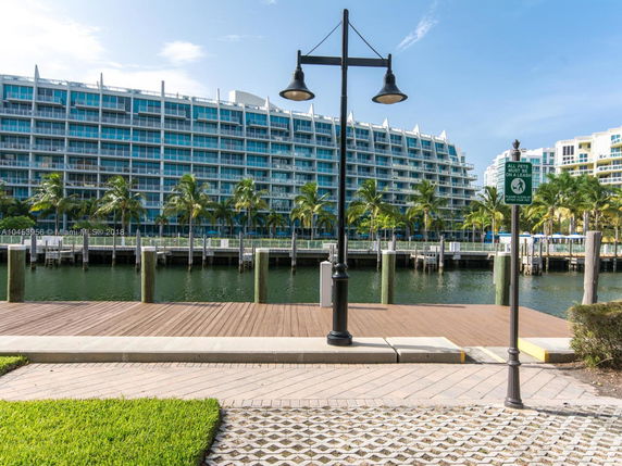 View of a modern multi-story waterfront building with numerous balconies and palm trees along the waterfront.