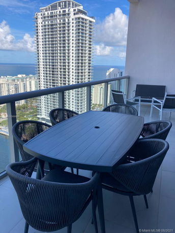 Balcony with black outdoor furniture overlooking high-rise buildings and the ocean in the distance.