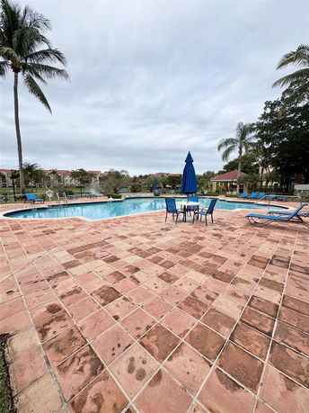 Outdoor swimming pool area with patio seating and palm trees.
