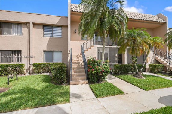 Front view of a two-story apartment building with exterior stairs and palm trees.