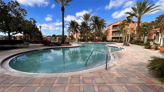 Outdoor swimming pool area in a residential complex with palm trees and paved surroundings.