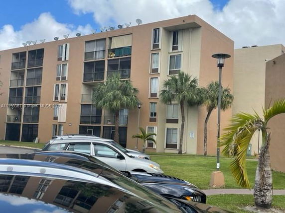 Front view of a multi-story apartment building with parking area and palm trees in front.