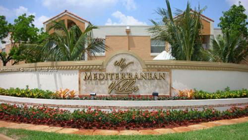 Front view of a Mediterranean-style villa with a sign and landscaped garden.