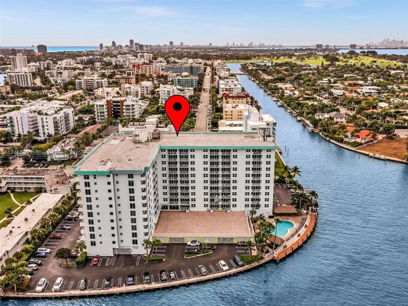 Aerial view of a high-rise building near a body of water with a flat rooftop, surrounded by a cityscape.