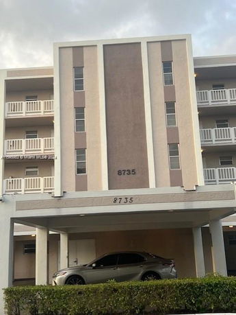 Front view of a multi-story building with a sheltered area and parked car.