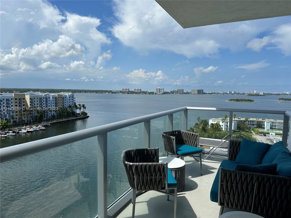 View from a balcony overlooking water and distant buildings, with patio seating.