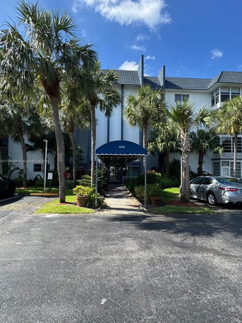 Front view of a multi-story building with blue awning and surrounding palm trees.