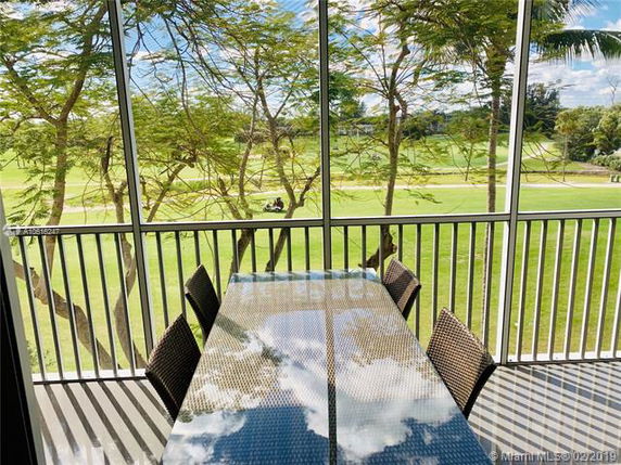 View from a balcony with a glass-top table and chairs, overlooking a golf course.