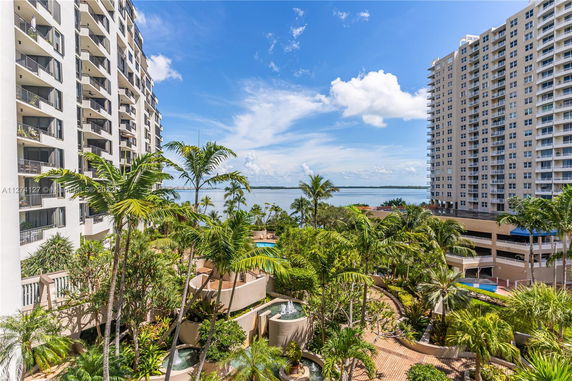 View of high-rise residential buildings with balconies and a lush garden area, overlooking a body of water.