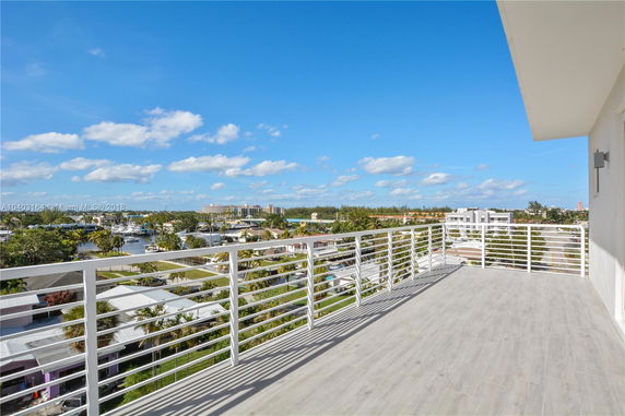 View from a building balcony overlooking a residential area with waterway and distant buildings under a blue sky.