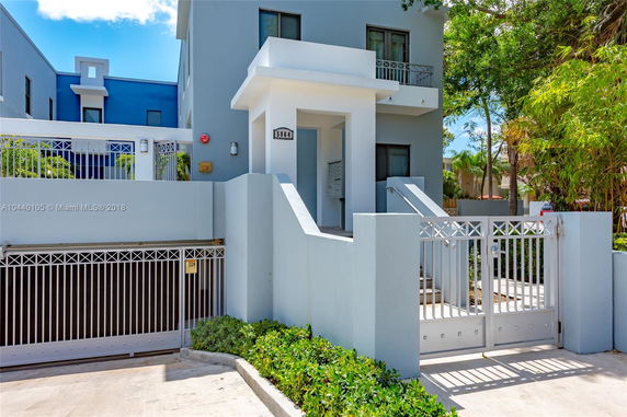 Front view of a modern multi-story building with a gated entrance and light blue facade.
