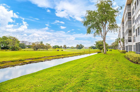 Side view of a multi-story residential building with a lush green lawn and a canal in the foreground.